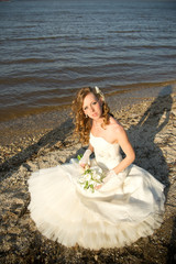 Fototapeta na wymiar Beautiful bride in a white dress on coast of river