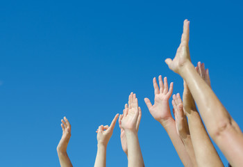Many hands raised up against the blue sky.