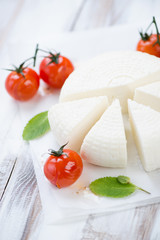 Vertical shot of sliced adygea cheese, baked tomatoes and mint