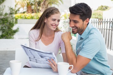 Smiling couple reading newspaper at café