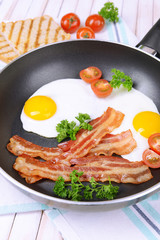 Scrambled eggs and bacon on frying pan on table close-up