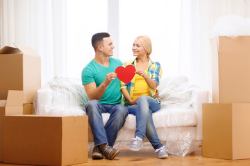 smiling couple with red heart on sofa in new home