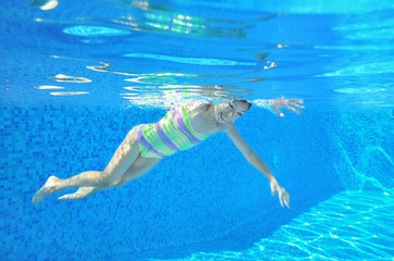 Happy active underwater child swims in pool, girl swimming