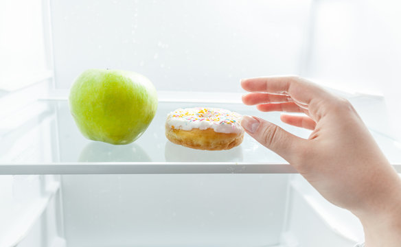 Hand Choosing Between Apple And Donut At Fridge