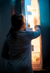 young woman opening refrigerator at night