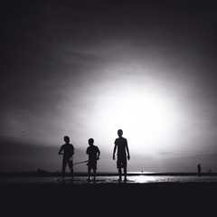 silhouette of three male friends walking on the beach