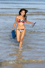 Girl with diving equipment running from the sea