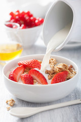 milk pouring over granola with strawberry for breakfast