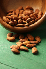 Almonds in bowl on color wooden background