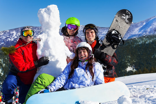 Four young people with snowboard and snowman