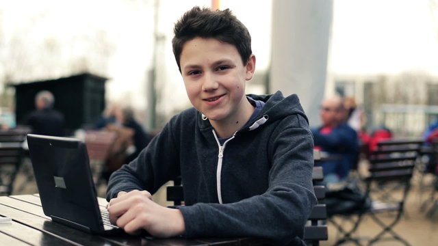Happy young teenager with laptop sitting in cafe