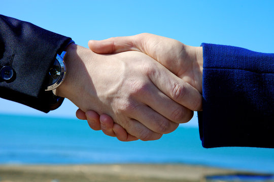 Hand shake between man and woman in front of the sea