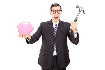 Scared businessman holding hammer and a piggybank
