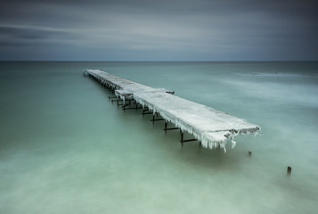 Winter landscape with old broken bridge among the stormy sea
