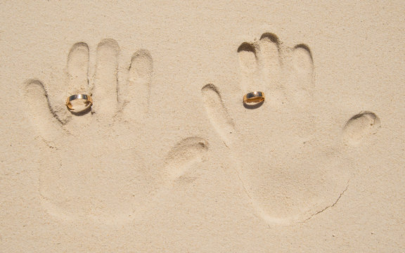 Hand print on sand beach with wedding rings.
