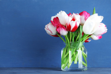 Beautiful tulips in glass jug on color wooden background