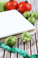 Notebook with measuring tape and vegetables on wooden