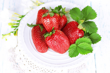 Strawberries with leaves on plate, on wooden background