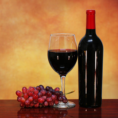 Wine Bottle and Glass of Red Wine with Fresh Grapes over beige