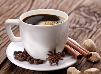 Cup of coffee with coffee beans and spices near it.