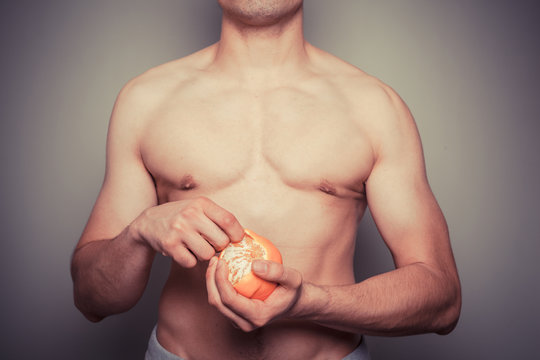 Athletic shirtless man peeling an orange