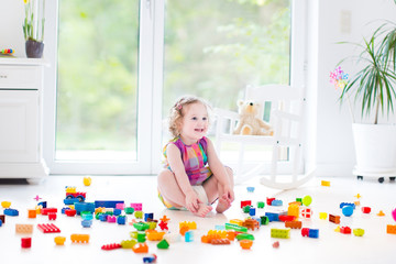 Adorable curly toddler girl playing in messing nursery