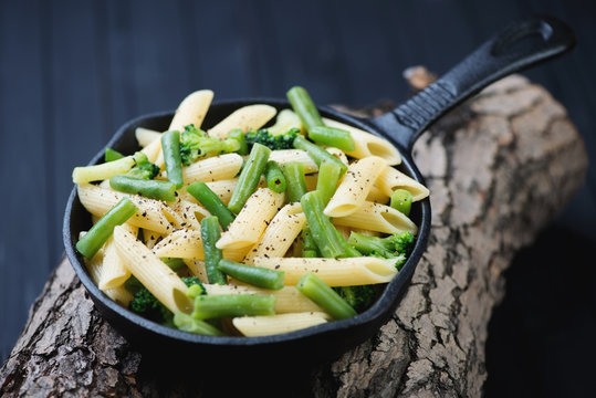 Frying Pan With Penne Pasta And Vegetables On Wooden Logs