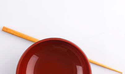 An empty bowl with a pair of chopsticks over white background