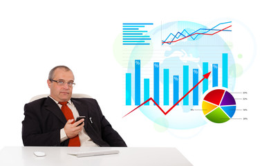 Businessman sitting at desk with statistics and holding a mobile
