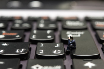 Obraz premium パソコンのキーボードに座って仕事をするミニチュアの人形