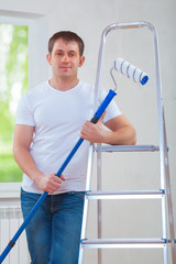 a young man holding paintroller and looking at camera