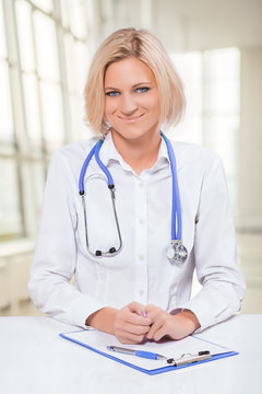 beautiful smiling female doctor sitting at white table and  look