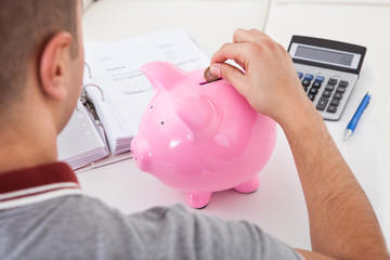 Rear view of young man putting coin into piggy bank