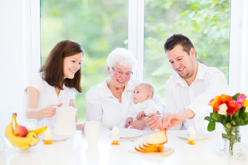 Young family with baby having breakfast with loving grandmother