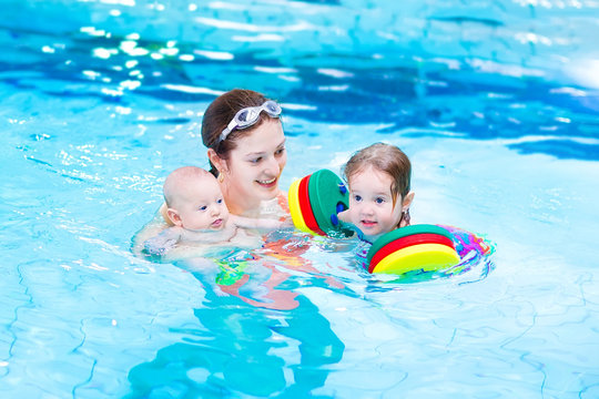 Young active mother swimming with toddler daughter and baby son