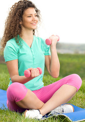 Beautiful young woman exercising with weights in the park.