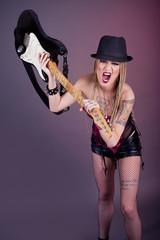 Young aggressive woman with tattoo smashing guitar