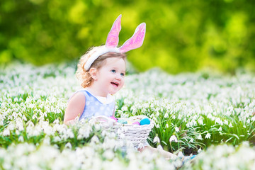 Adorable toddler girl wearing bunny ears in first spring flowers