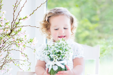 Beautiful curly toddler girl with bouquet of snowdrops
