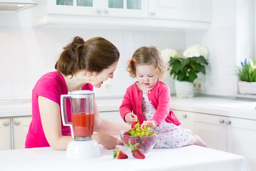 Laughing toddler girl and beautiful mother making breakfast