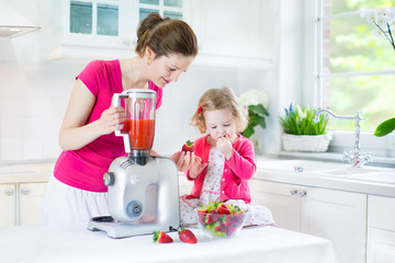 Toddler girl with her beautiful young mother making fresh juice