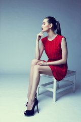 young elegant woman in red dress sit on stool, studio shot