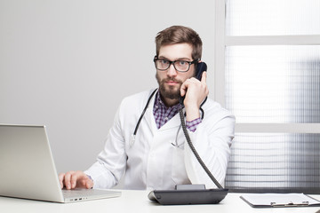 Doctor using phone and computer while at work