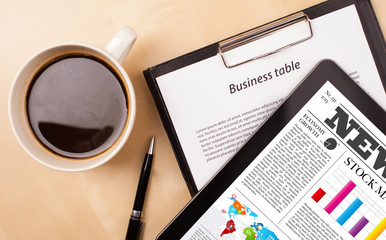 Tablet pc shows news on screen with a cup of coffee on a desk