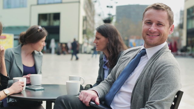 Businessman smiling to camera and sitting with colleagues in str