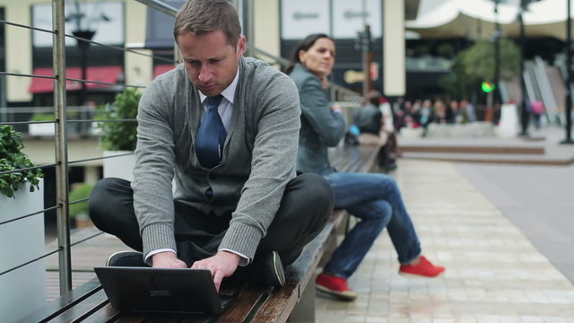 Businessman sitting on street bench and working on laptop, stead