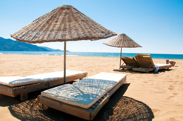 Sunbeds and rattan parasols on sandy seaside.