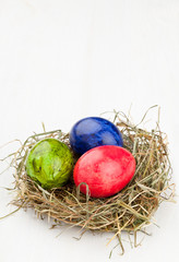 Easter eggs in hay nest on white wood