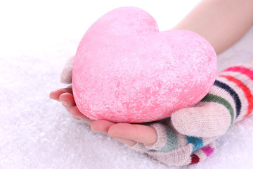 Female hands in mittens with heart on snow background