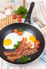 Scrambled eggs and bacon on frying pan on table close-up